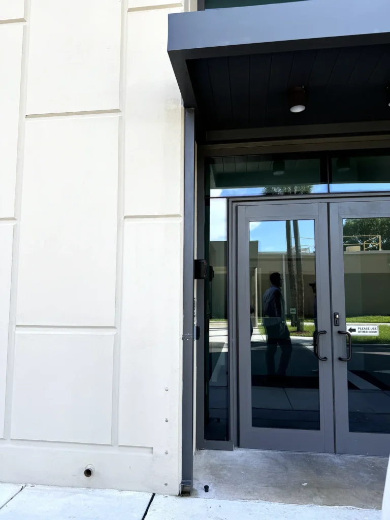 Dark aluminum canopy above the sheriff’s office main entrance, beside a glass facade and landscaped walkway.