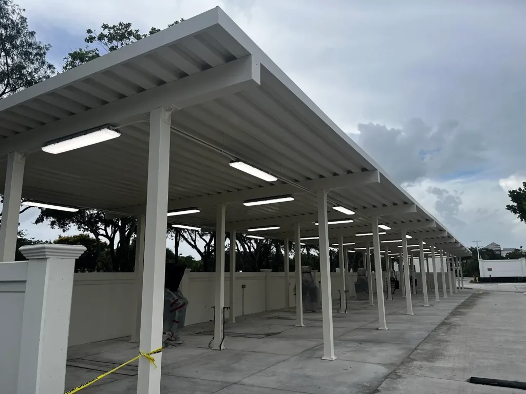 Detailing equipment beneath the white aluminum canopy, with roof framing, overhead lights and a vehicle in the background.