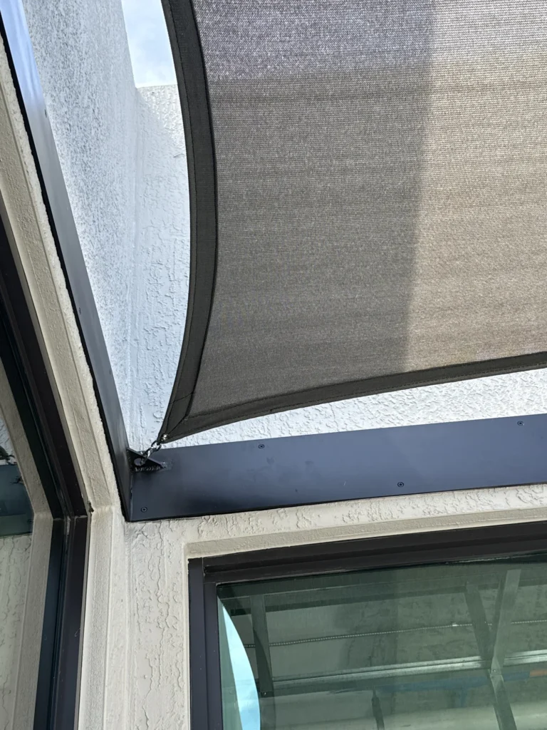 Close-up of a shade sail attachment at the building corner above a window.