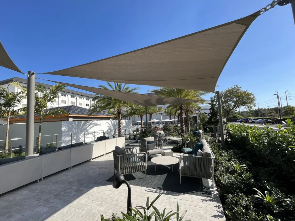 Overlapping triangular shade sails above outdoor sofas, with palm trees beyond the terrace.