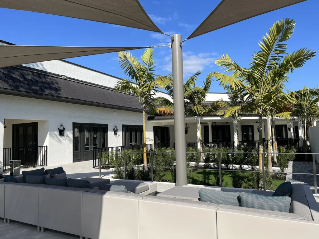 Triangular shade sail stretched between metal posts above a paved terrace with lounge seating.